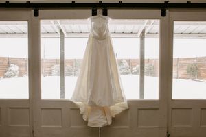 A elegant white wedding dress hanging on a barn door against snowy winter windows.