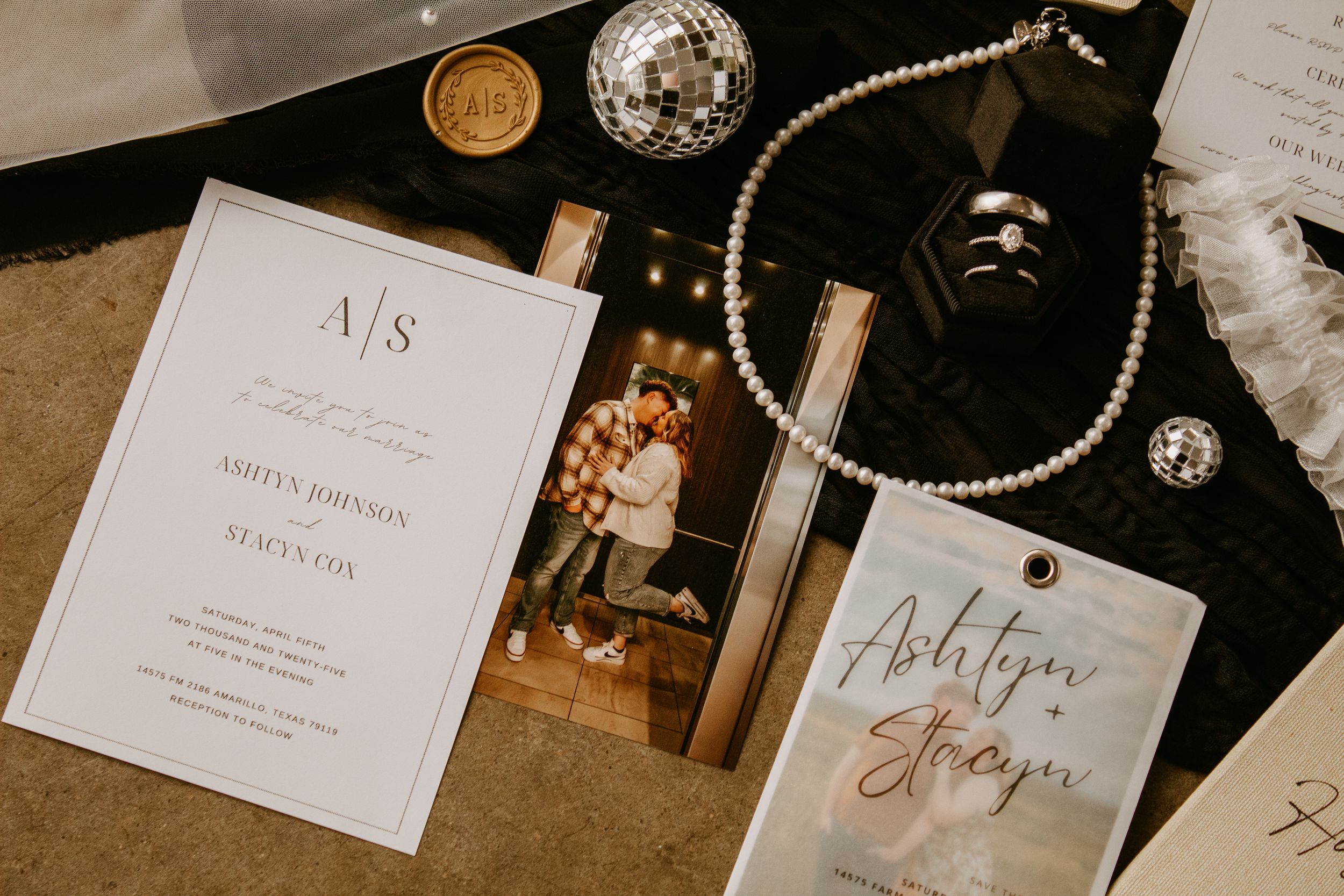 Elegant wedding invitation suite with monogram, couple photo, pearl necklace, disco ball, and calligraphy name cards on dark surface.