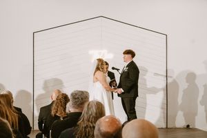 Bride and groom exchange vows at modern wedding ceremony with minimalist geometric arch backdrop and seated guests.