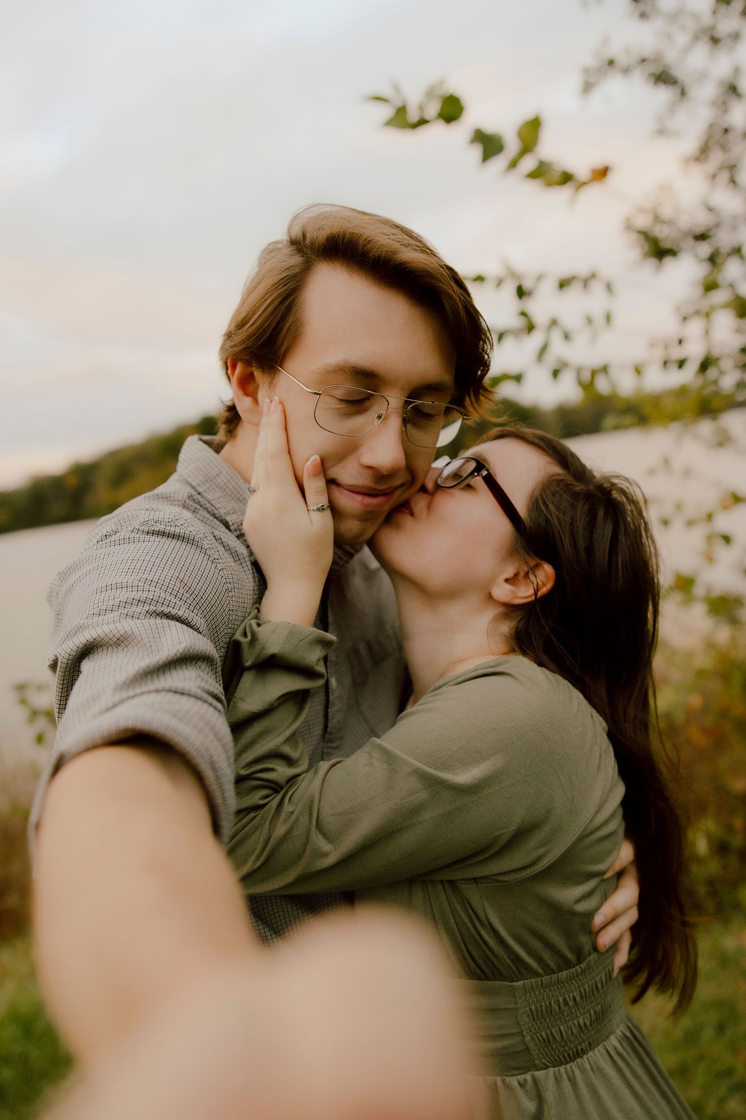 Couple sharing a tender kiss outdoors near a lake, woman in green dress holding mans face gently.