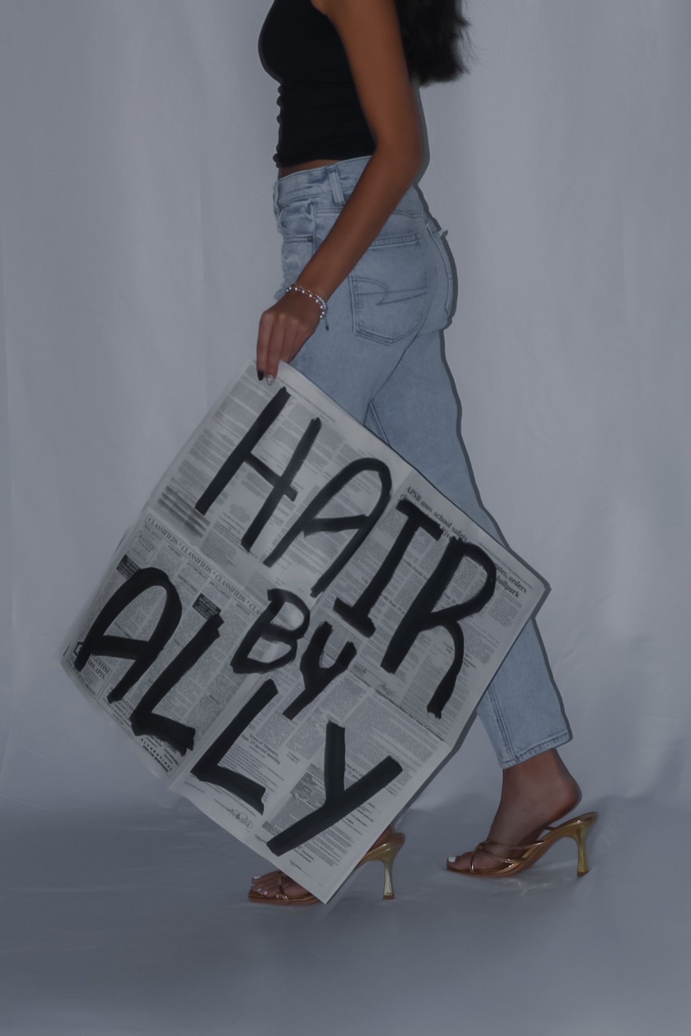 Person in black top and jeans holding up a large white sign with text.