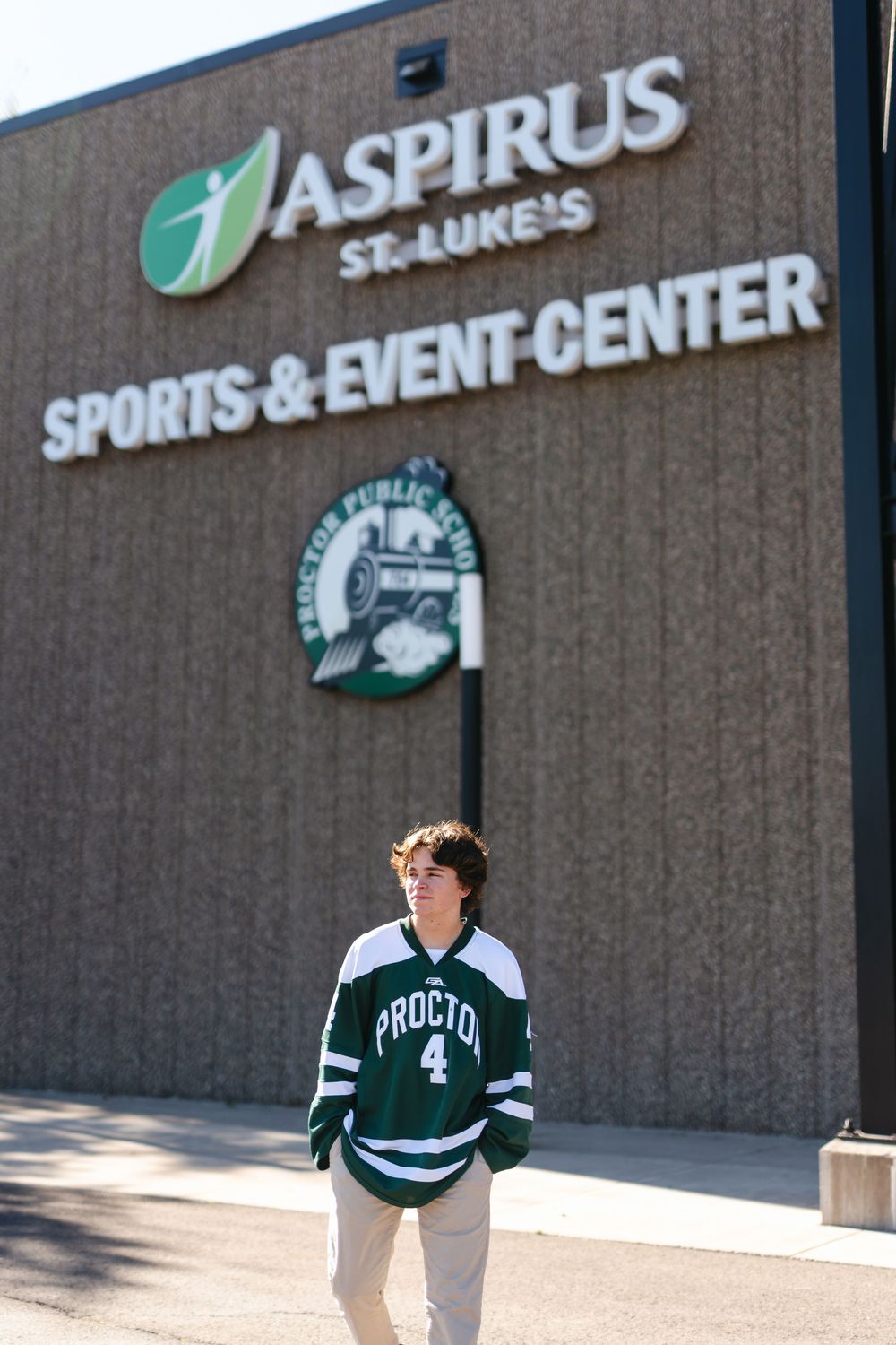 Student poses in front of Aspirus Sports & Event Center wearing a green and white hockey jersey.
