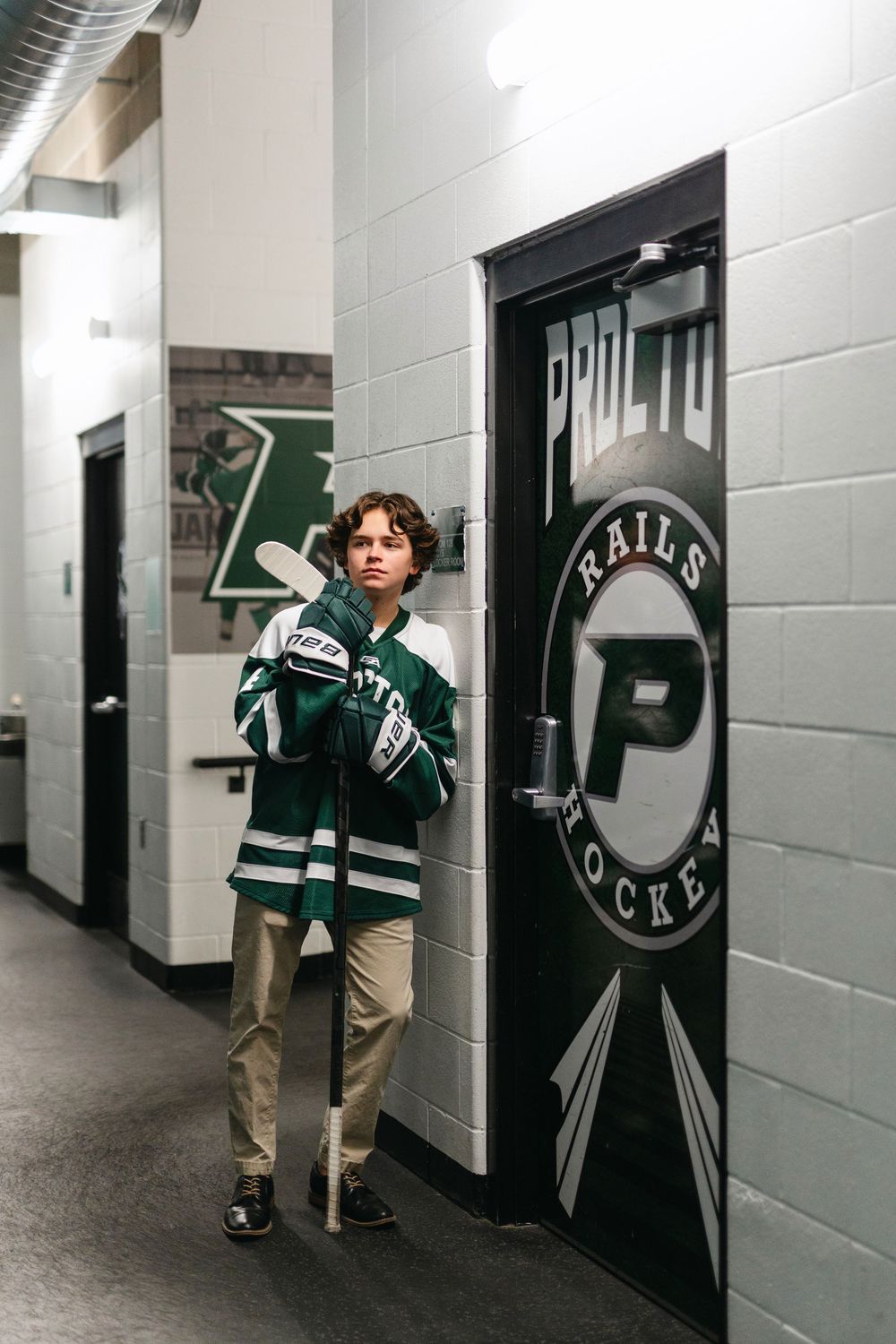 A hockey player explores the arena hallway with lockers and team logos on the walls.