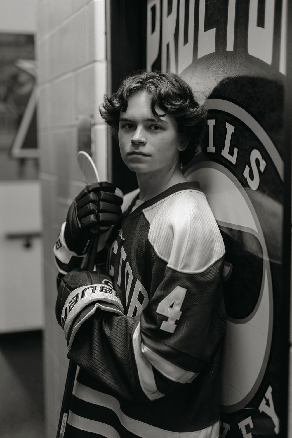 A black and white sports portrait in a hockey jersey against a team logo background.