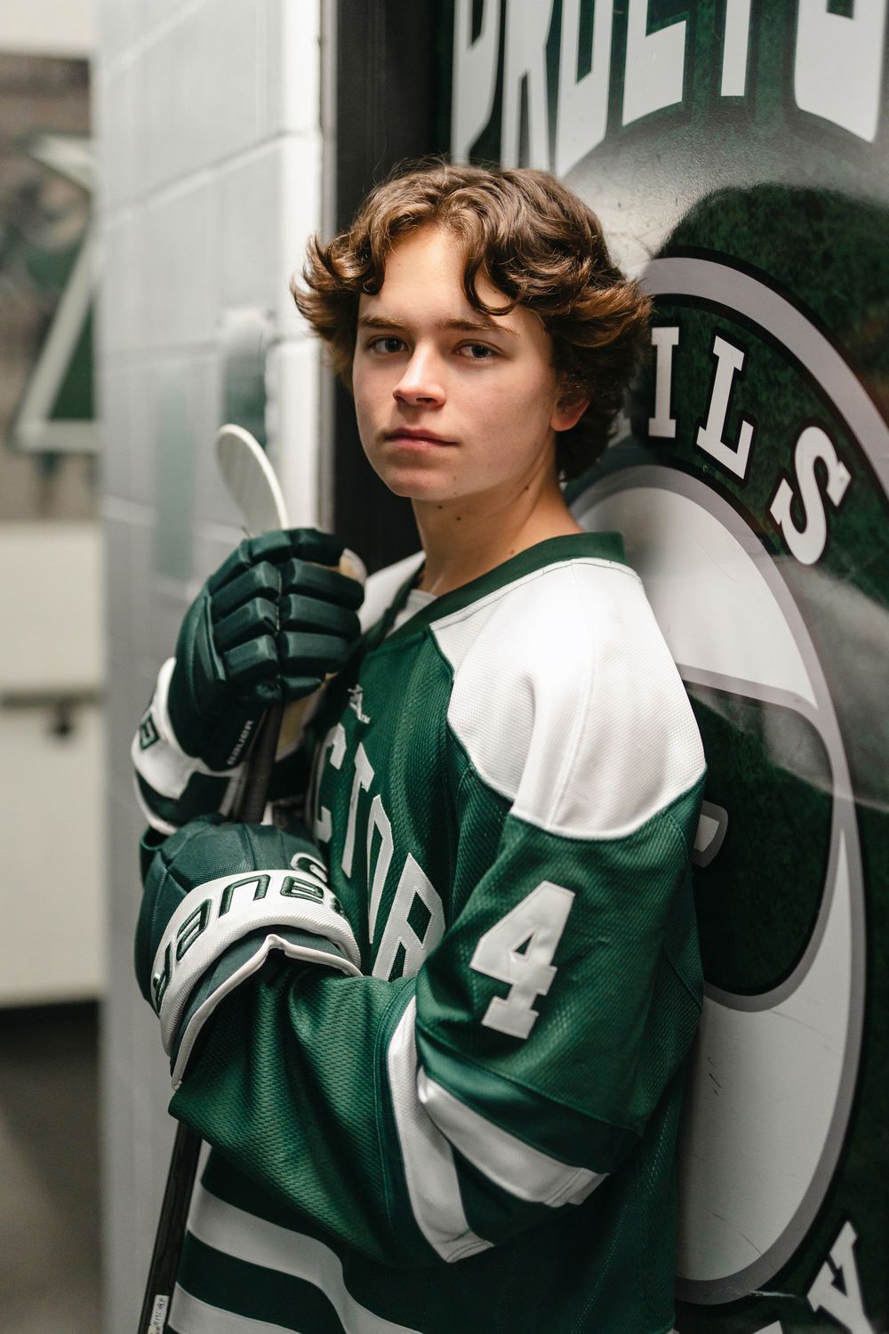 An athletic portrait in a green and white hockey jersey with number 4 against a team logo.