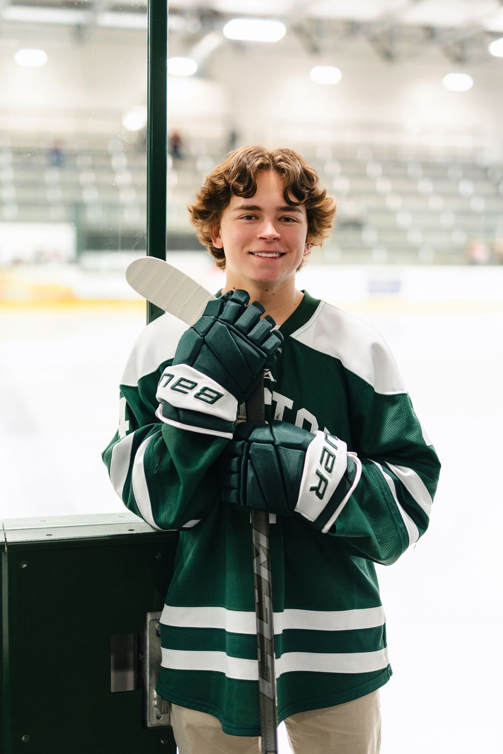 A hockey player in a dark green and white jersey smiles while standing near a microphone podium.