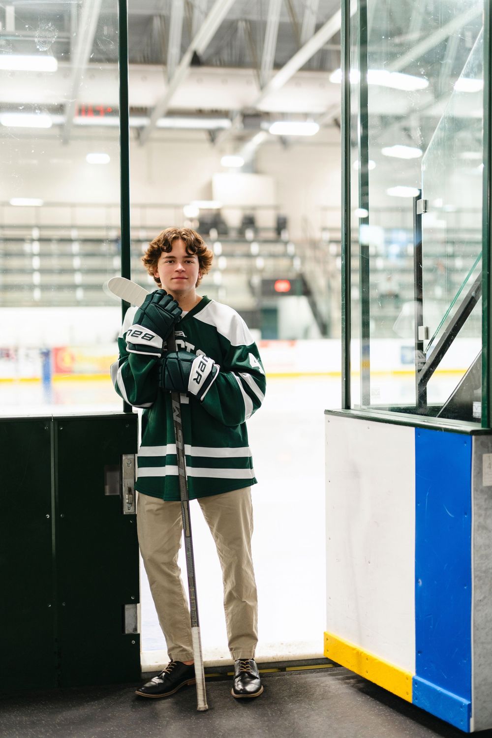 A person in hockey gear stands near glass panels overlooking an ice rink.