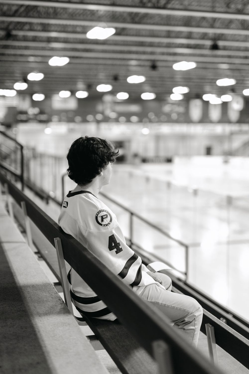 Black and white photo of a hockey player sitting alone in empty arena bleachers wearing jersey number 4.