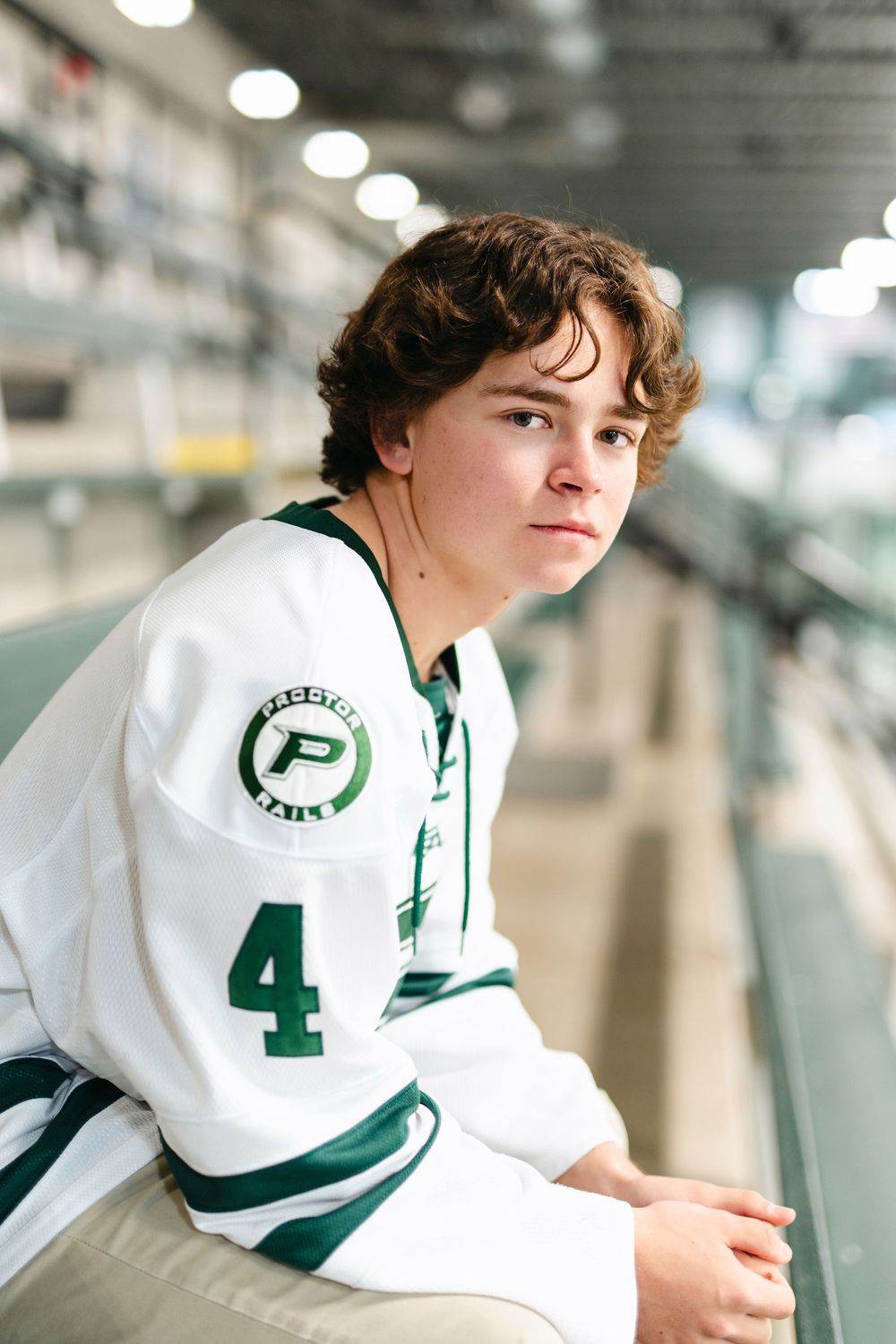 A student athlete wearing a white and green varsity jersey with number 4 sits in what appears to be a sports facility.