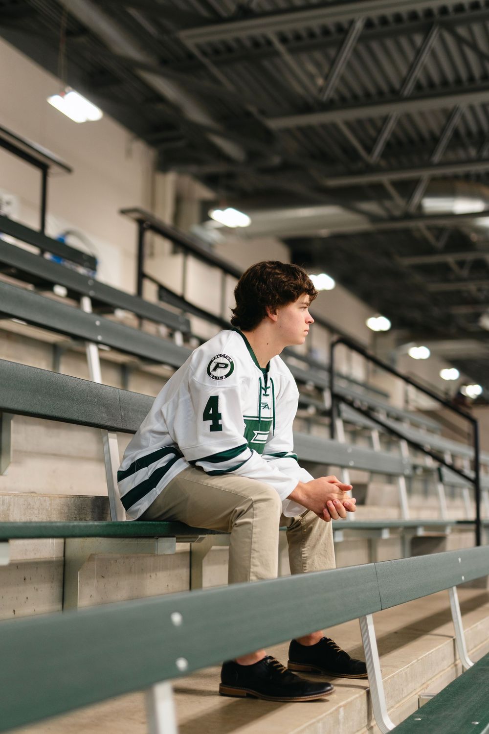 A hockey player leans against the arena bleachers while wearing a white and green jersey.
