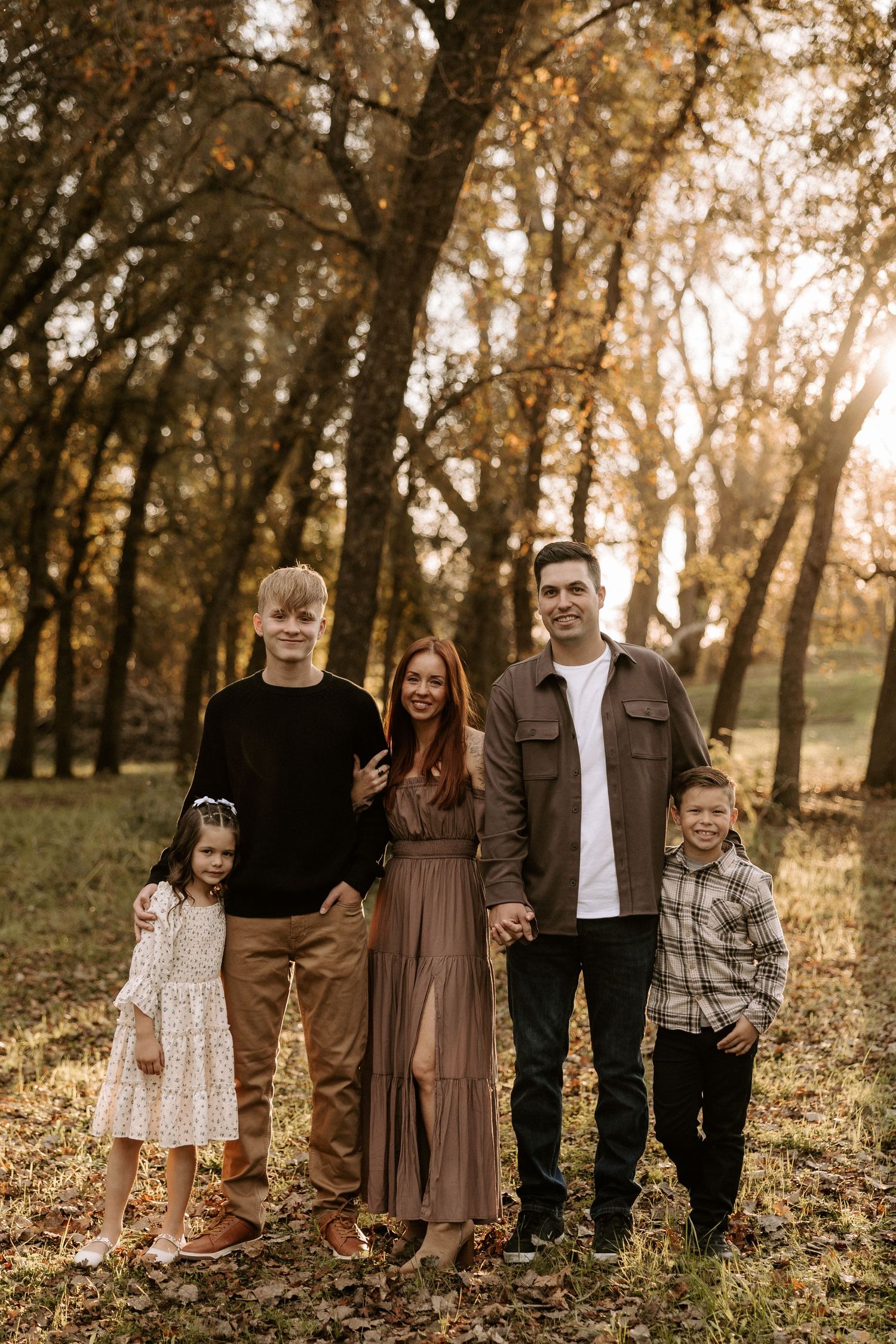 A group poses together in a wooded area during golden hour with autumn trees creating a warm, natural backdrop.