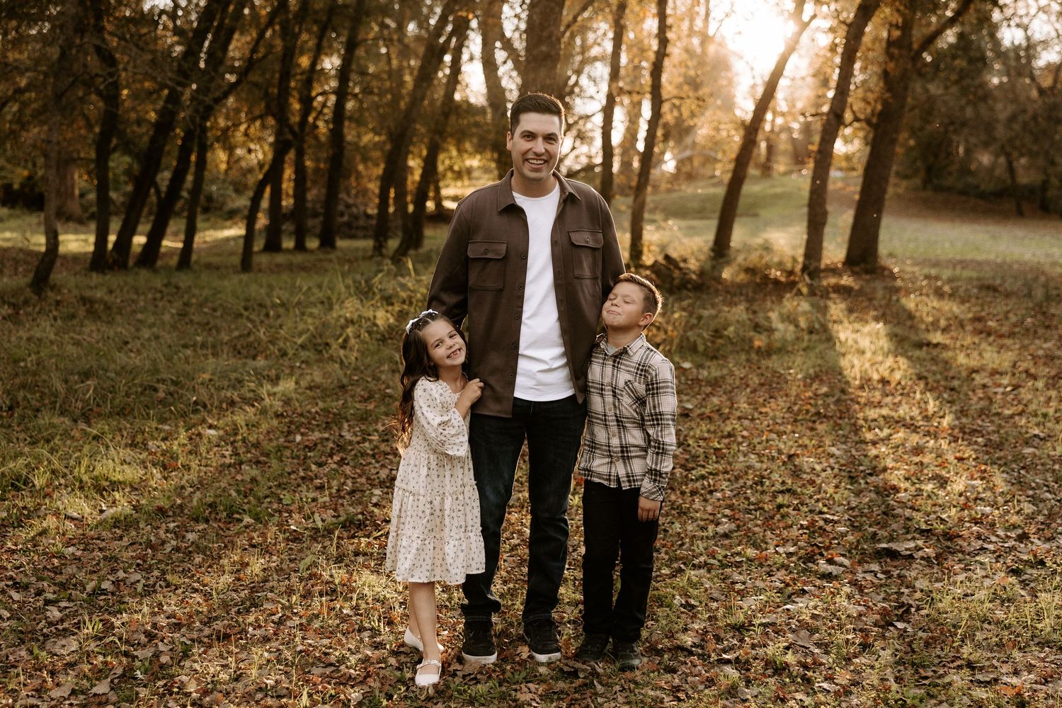 Family walks together through a sunlit autumn forest path covered in fallen leaves during golden hour.