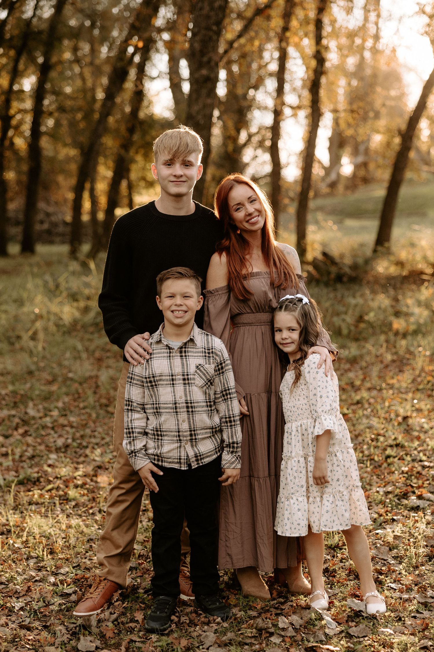 A family poses together in a wooded area during golden hour with autumn trees in the background.