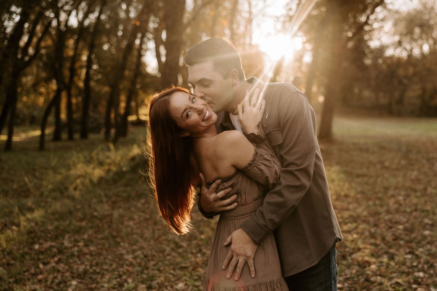 A romantic couple embraces in a sunlit autumn forest during a golden hour photoshoot.