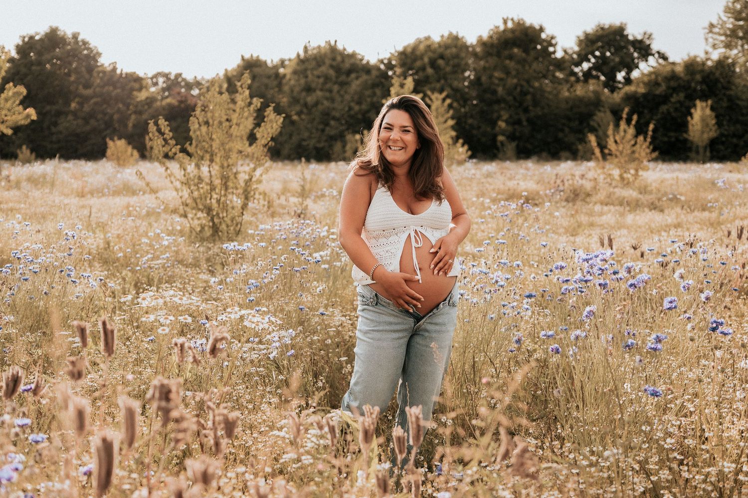 Een zwangerschapsshoot in een open veld in Roeselare, Zonnebeke, Ieper met een casual jeansbroek aan en een gehaakte top voor de buik.