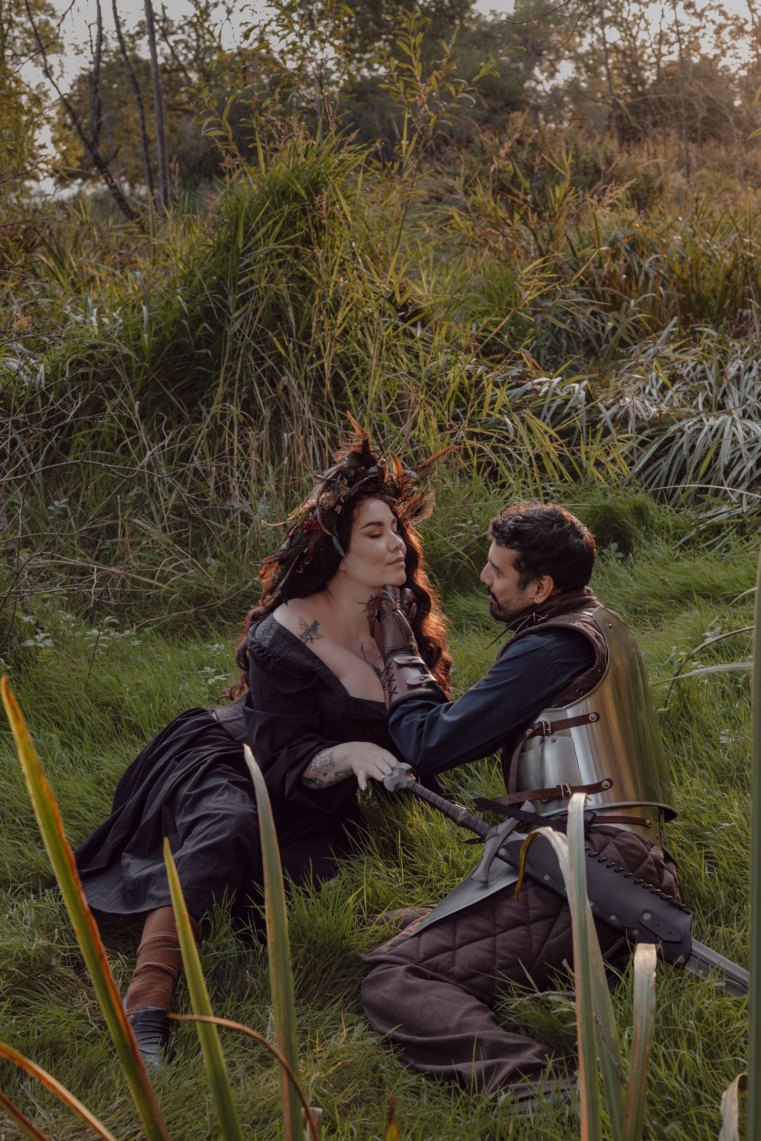 Witch and knight pose in the tall grass for their engagement session in Stanley Park, Vancouver, BC bringing fantasy to their life.