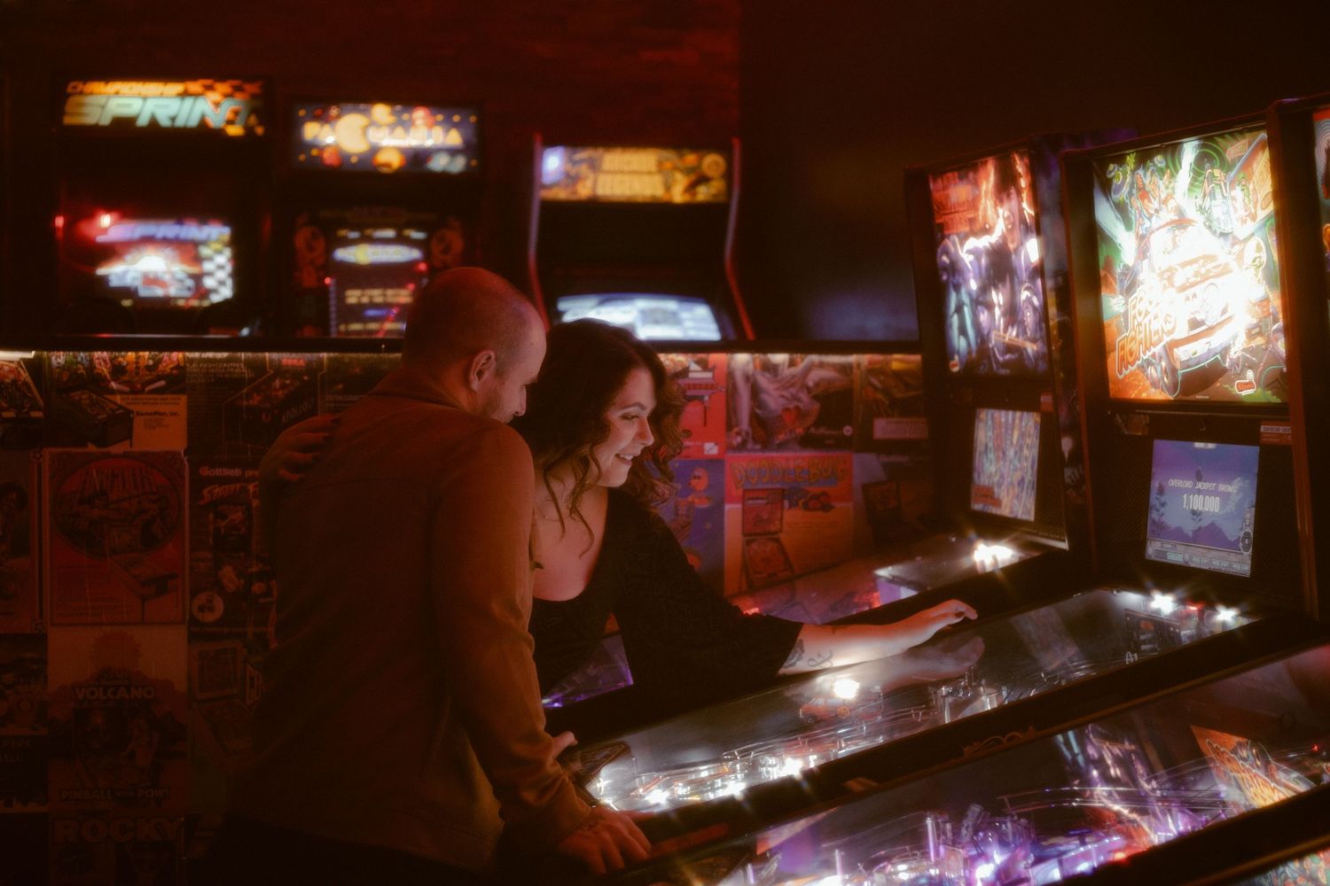 An engagement session that has fun, vintage vibes at an arcade in London, Ontario. The couple playing together at a pinball machine.