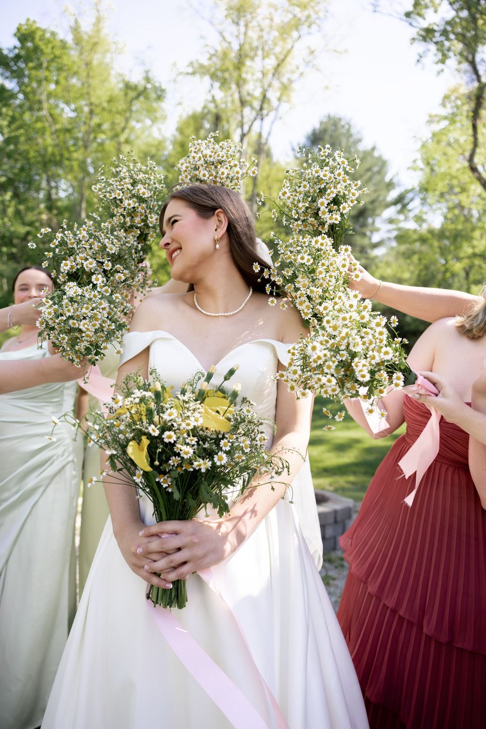 Wedding party in burgundy and white dresses holding delicate white floral bouquets while celebrating outdoors.