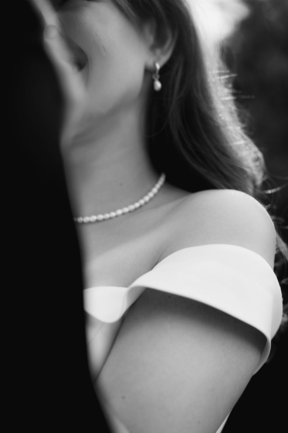 Black and white portrait showing an elegant pearl necklace and off-shoulder dress with dramatic lighting and shadows.