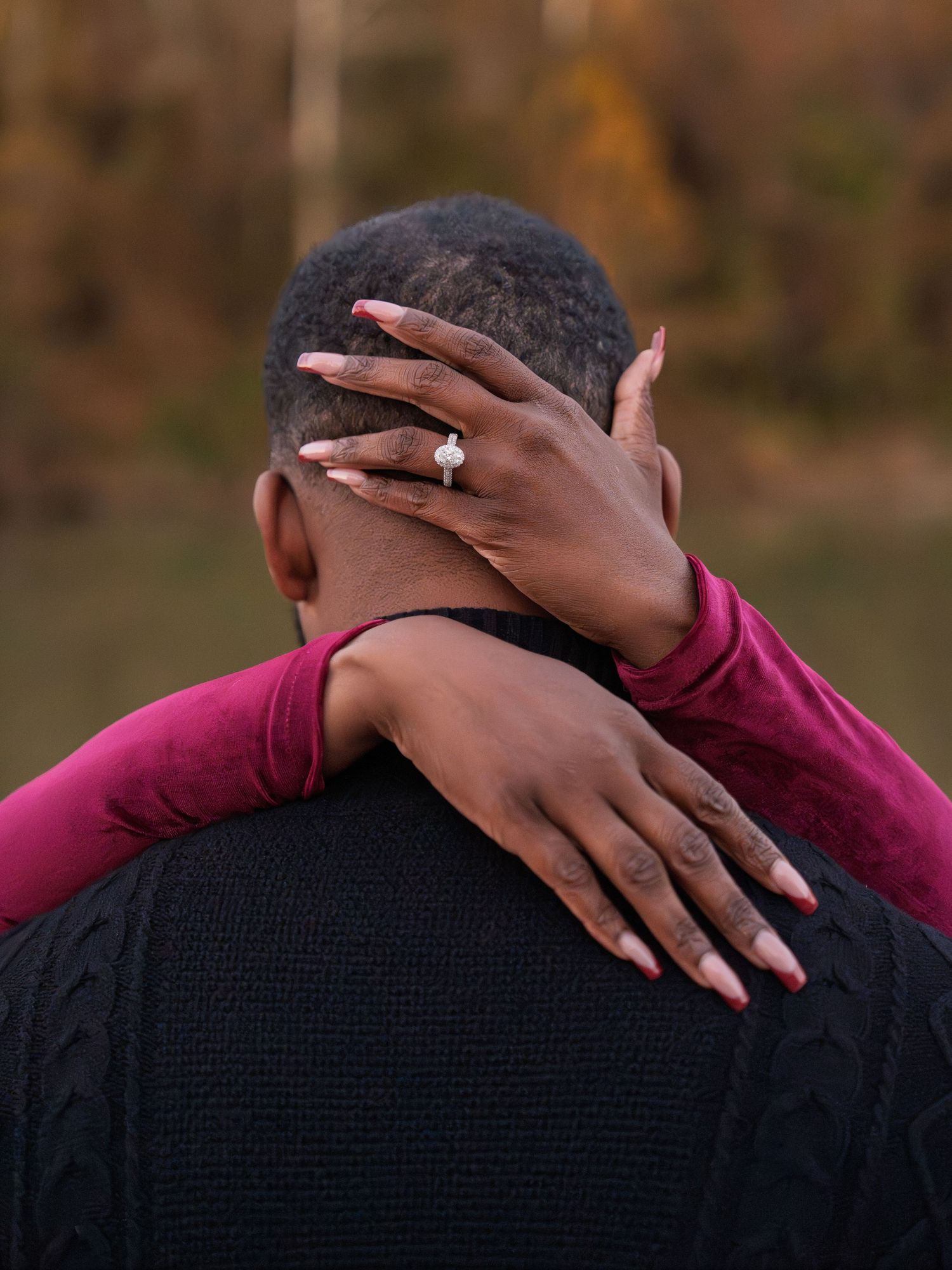 A sparkling engagement ring is showcased as hands embrace against a black sweater background.