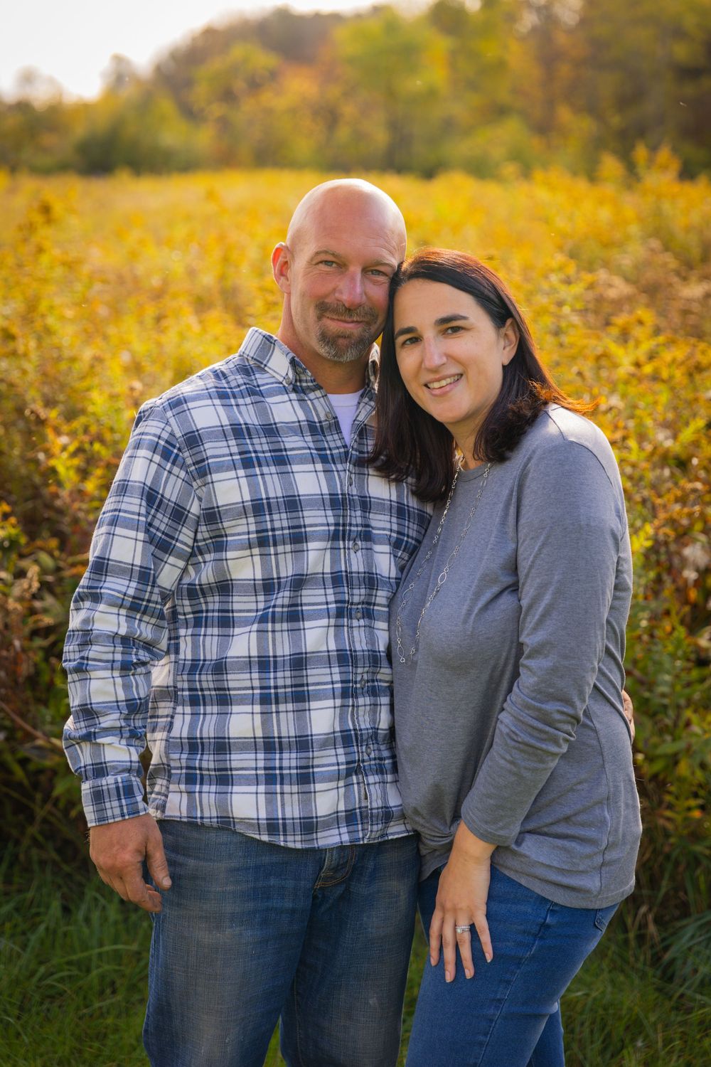 Smiling couple embracing in front of a golden autumn field at sunset.