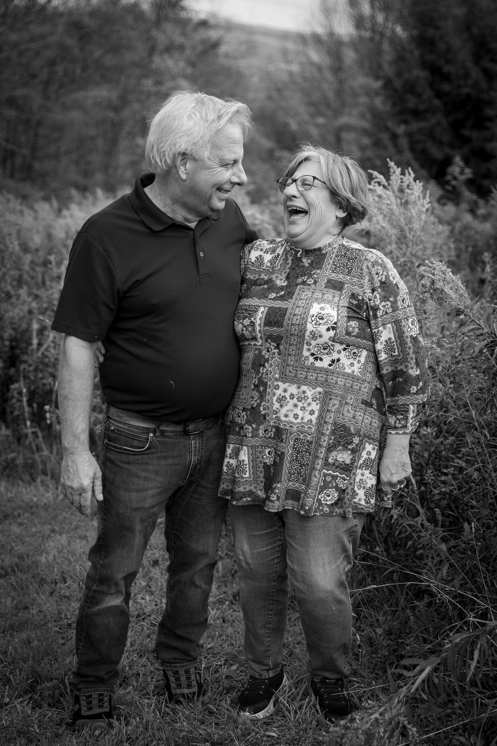 Black and white photo of an older couple laughing joyfully together outdoors in nature.