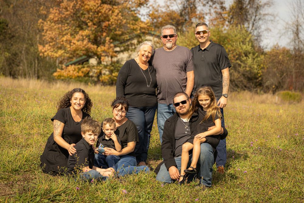 Extended family of eight posing together in a sunny autumn field with colorful fall foliage.