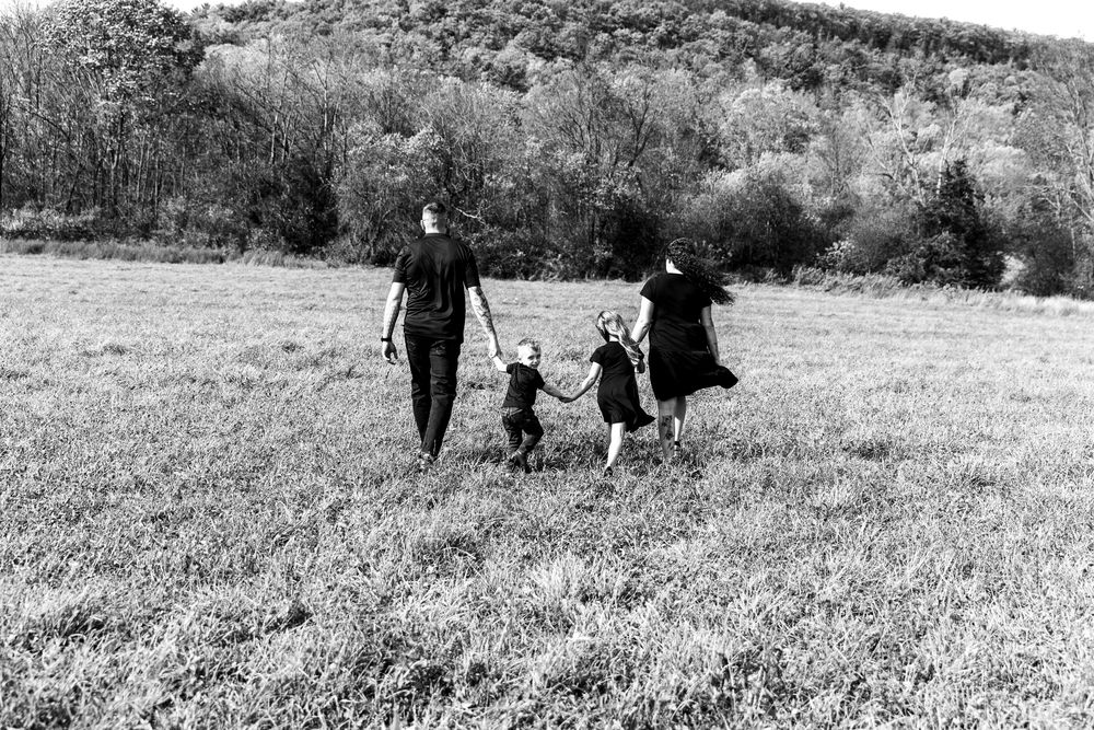 Black and white photo of family of four holding hands walking through an open meadow.