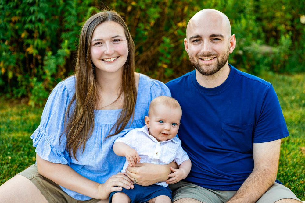 Smiling young couple sitting outdoors on grass with their happy baby boy.