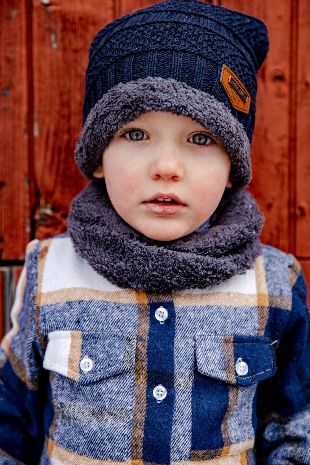 Adorable toddler boy wearing navy knit beanie and gray fleece infinity scarf with plaid jacket in winter.