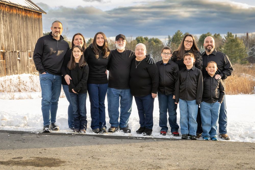 Large multigenerational family group portrait outdoors in matching black outfits during winter snow.