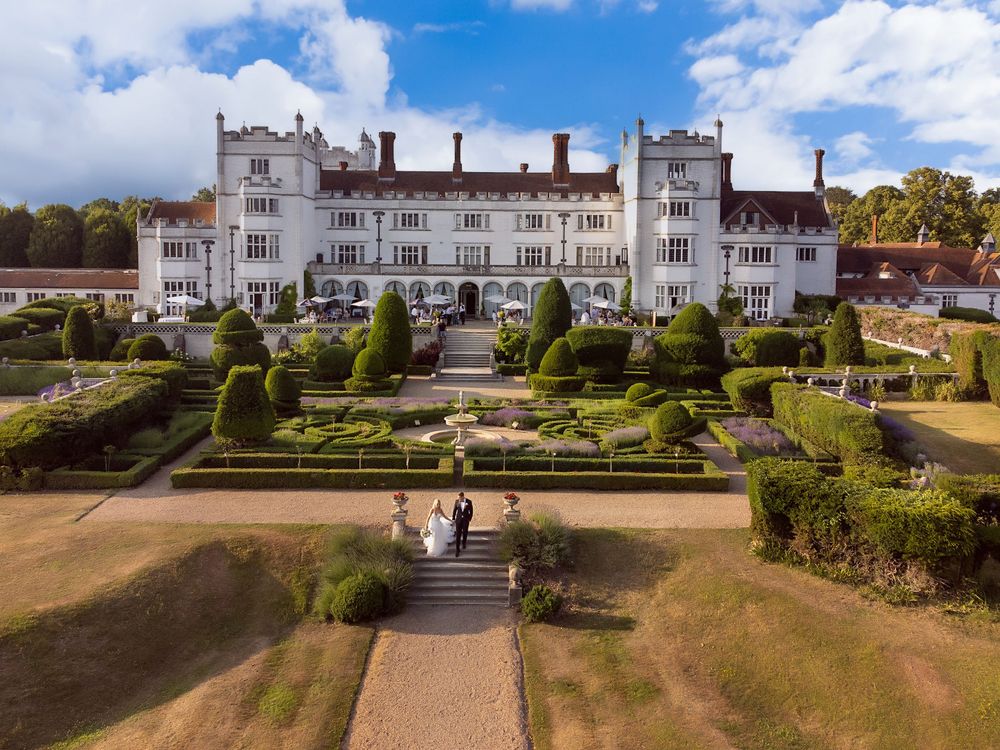 Aerial panoramic view of a grand white mansion with manicured gardens and pathways leading to the estate.