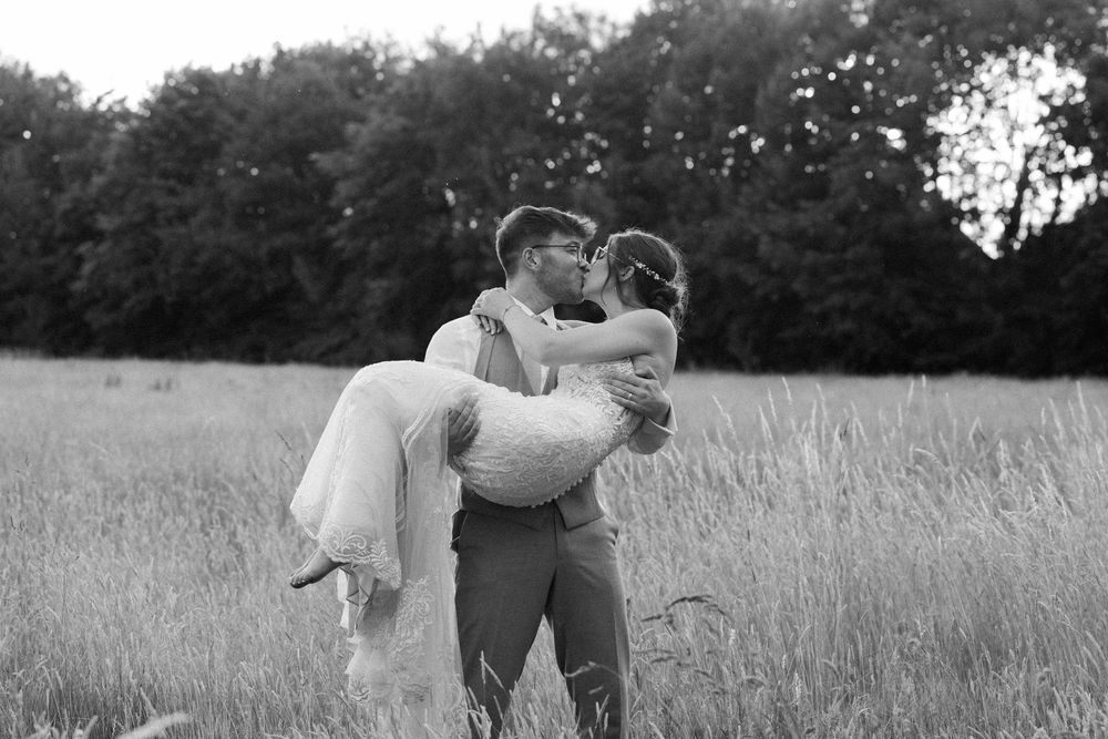 A couple shares a romantic kiss in a tall grass meadow during a summer evening.