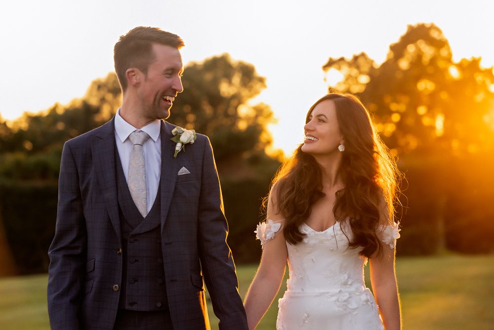 A couple shares romantic moments at sunset in a grassy field during their wedding photoshoot.