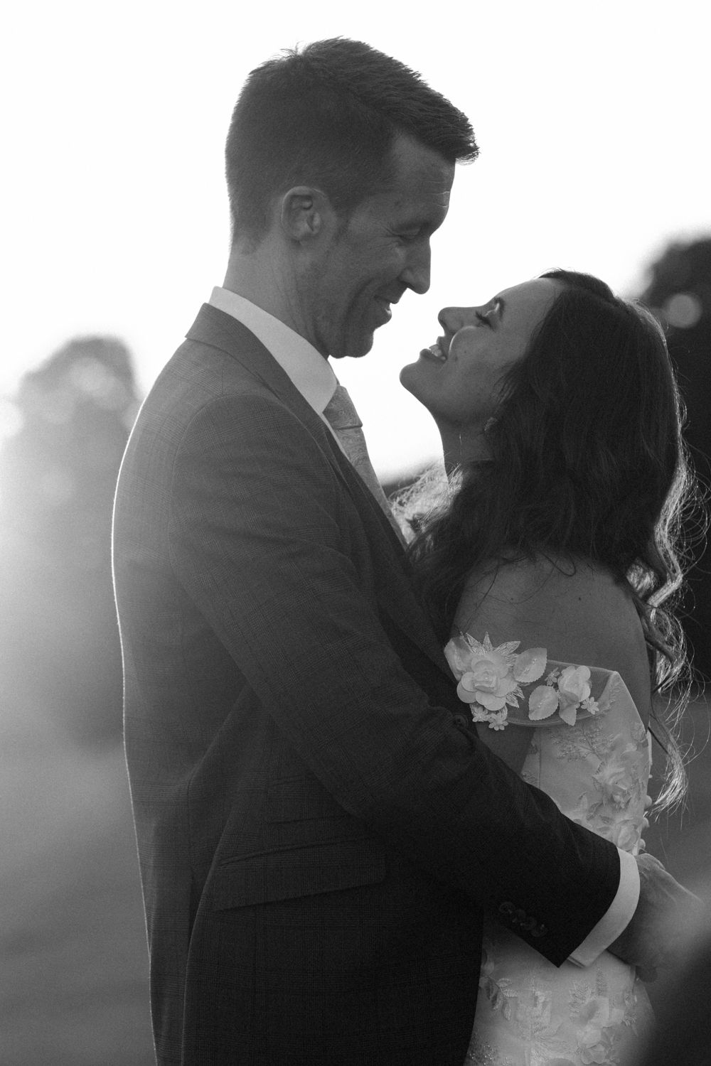 A romantic black and white wedding photo of a couple embracing in soft sunlight.