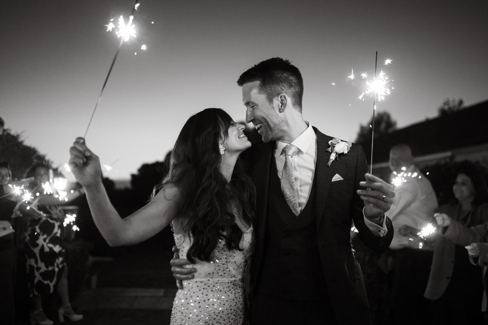 Wedding guests hold sparklers creating a magical nighttime celebration atmosphere at an outdoor reception.