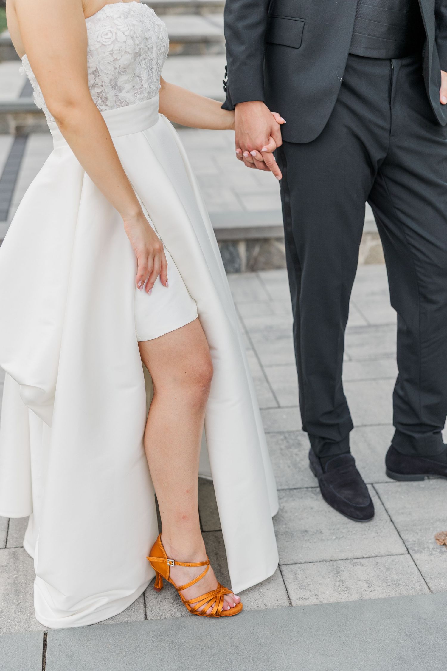 Close-up of wedding attire showing white dress with orange shoes and black suit.