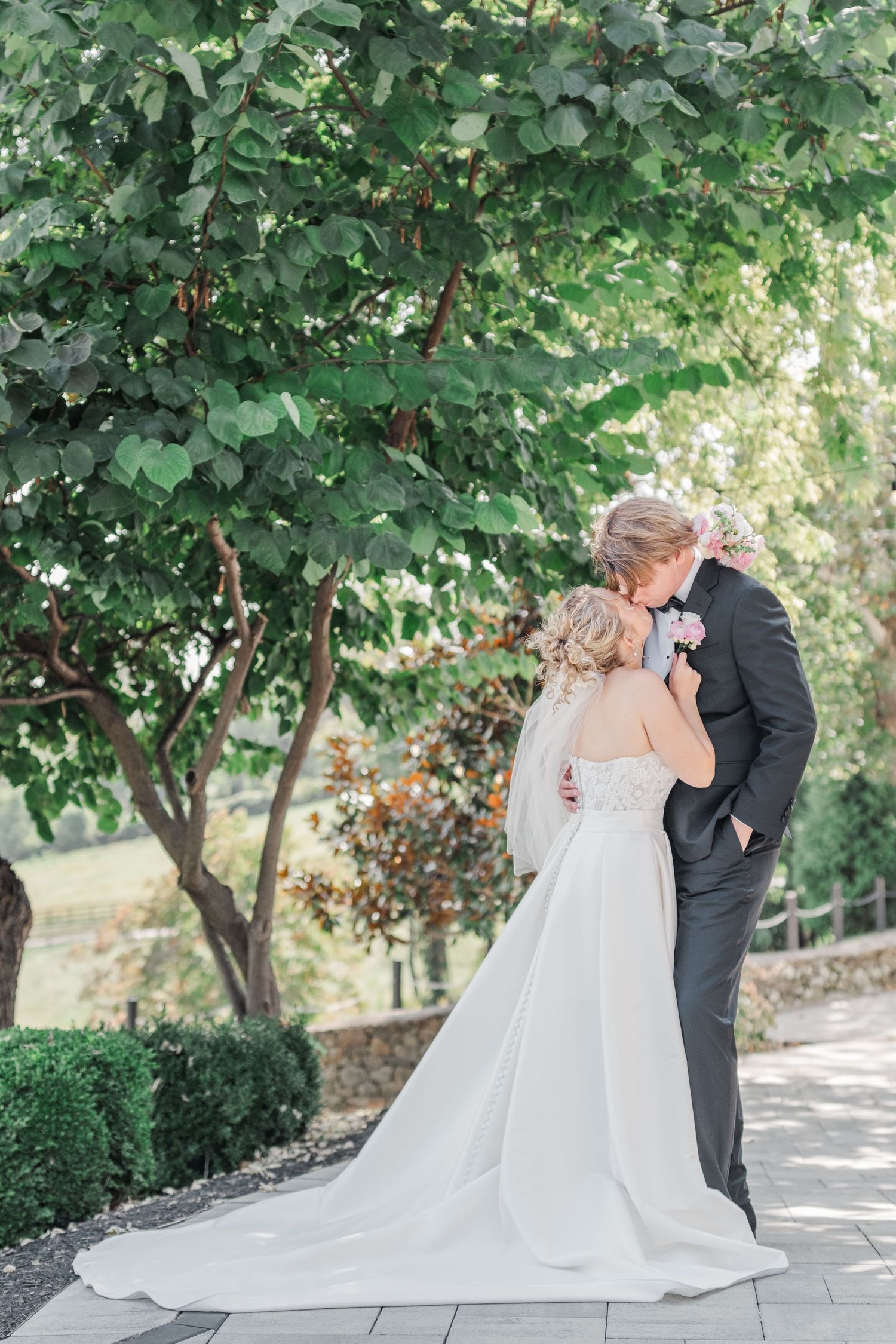 A tender embrace between newlyweds on a stone pathway surrounded by trees.