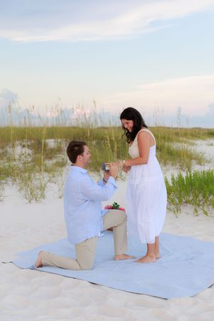 A romantic beach proposal sequence showing a couple on a blue blanket during sunset.
