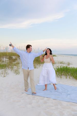 A joyful couple celebrates their beach engagement with excited poses on the sand.