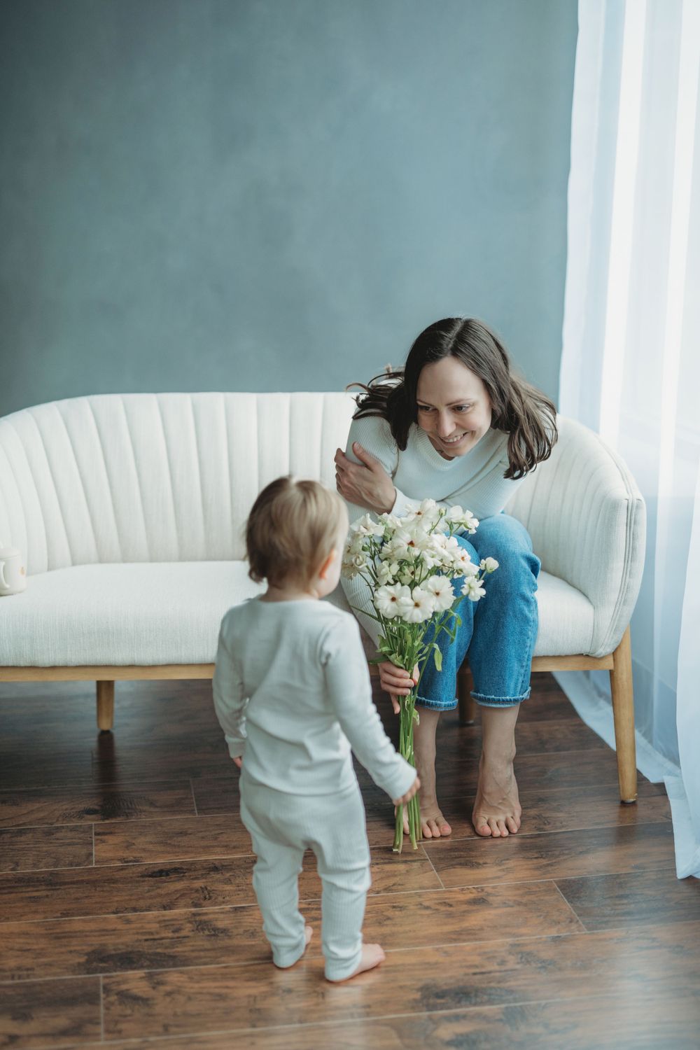 Sweet interaction between parent and toddler with white flowers in a minimalist living room setting.