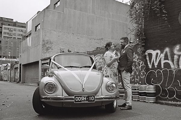 A classic Volkswagen Beetle parked in an urban setting with graffiti-covered walls in the background.