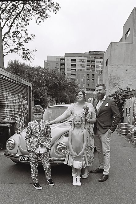 A sequence of black and white photos showing people posing playfully by a vintage car on a street.