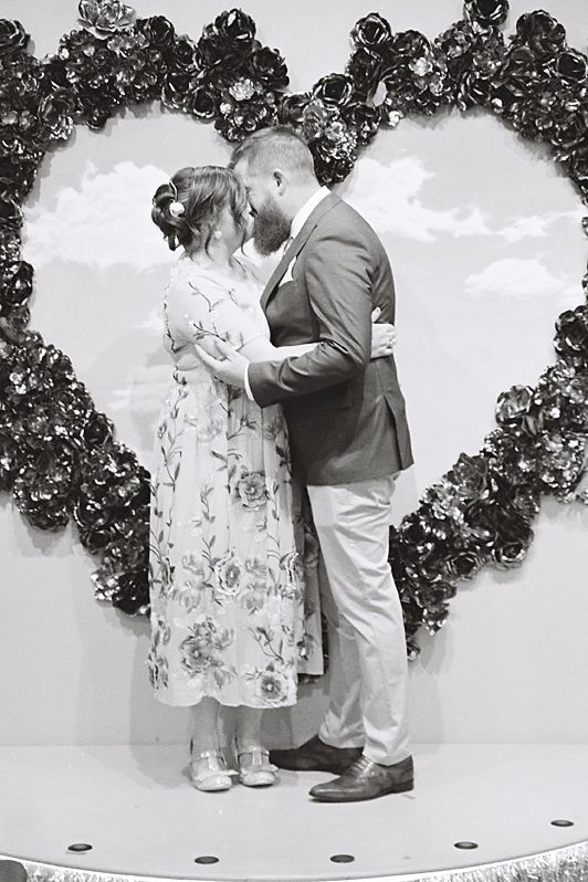 A sequence of black and white photos showing a couple in formal attire sharing romantic moments against a floral backdrop.