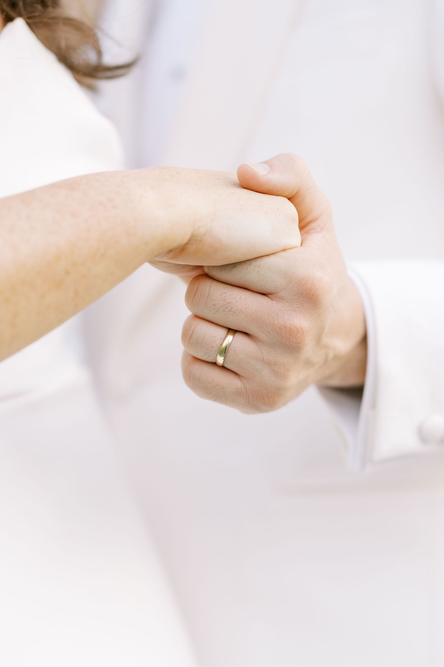 Close-up of hands with a gold wedding band ring against a soft white background.