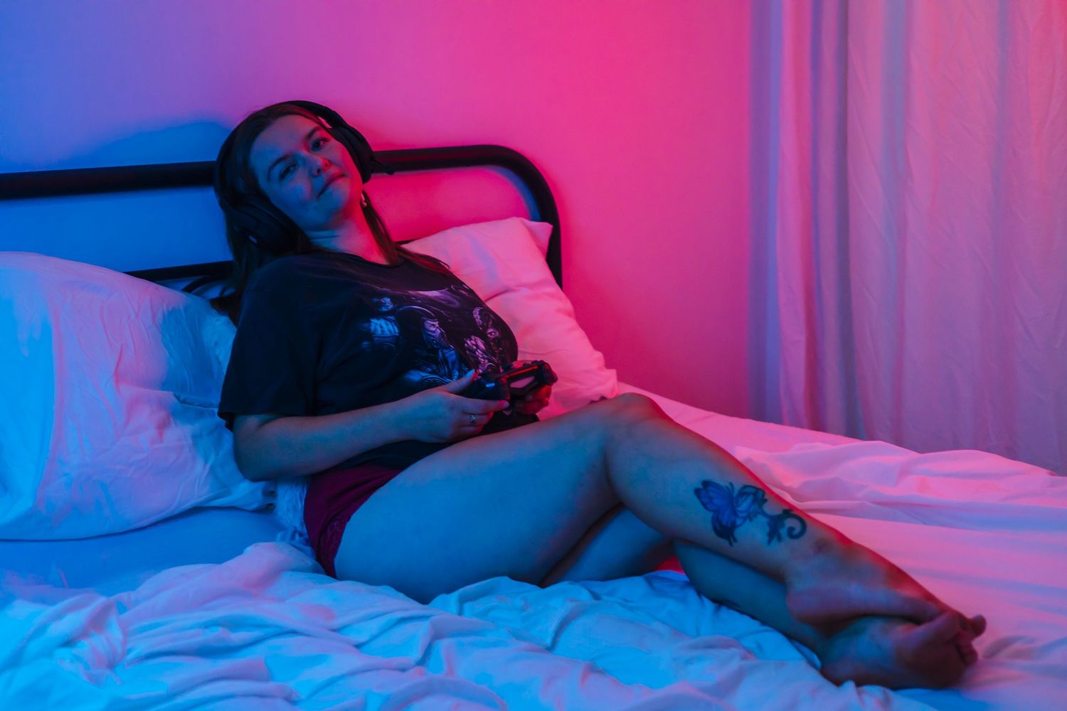 Dramatic neon pink and blue lighting illuminates a bedroom scene with someone relaxing on white bedding.