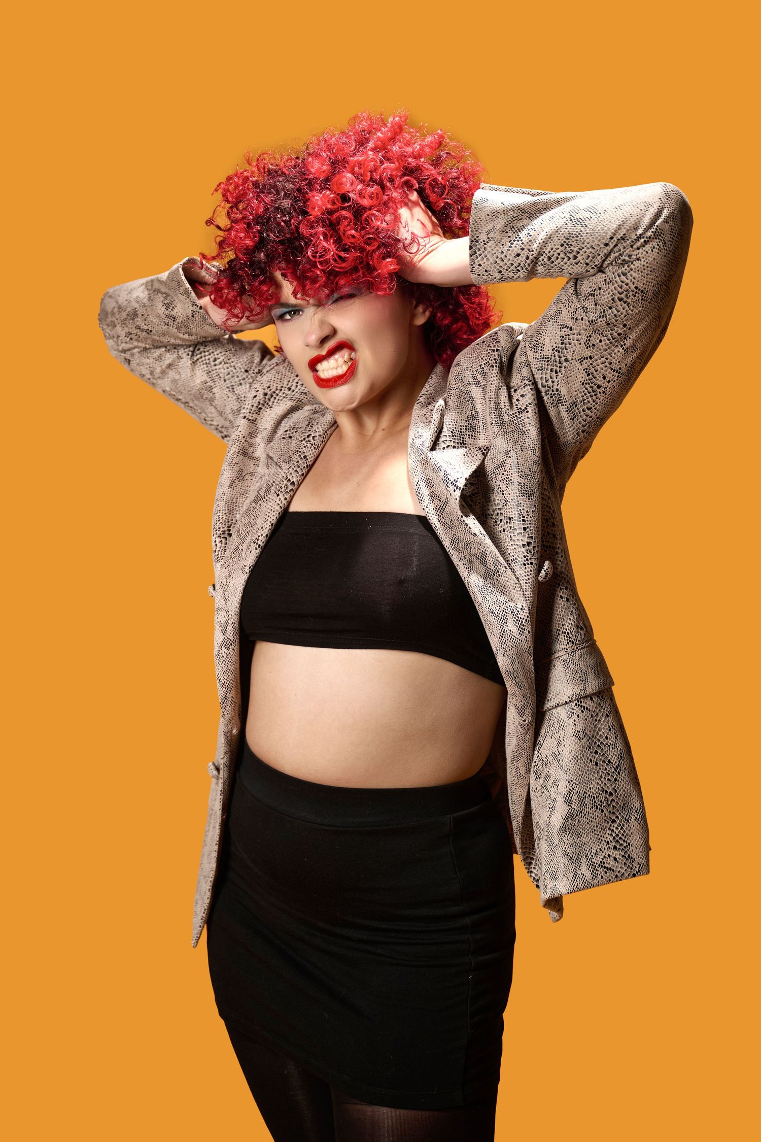 Fashion photo with snakeskin jacket, black crop top and skirt, bright red hair against orange background.