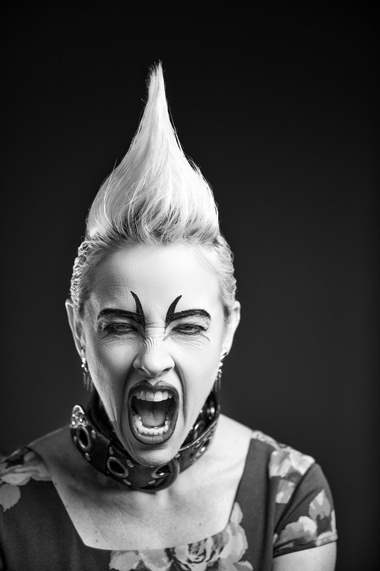 Dramatic black and white portrait showing spiked white mohawk hair, bold face paint and expressive screaming pose.