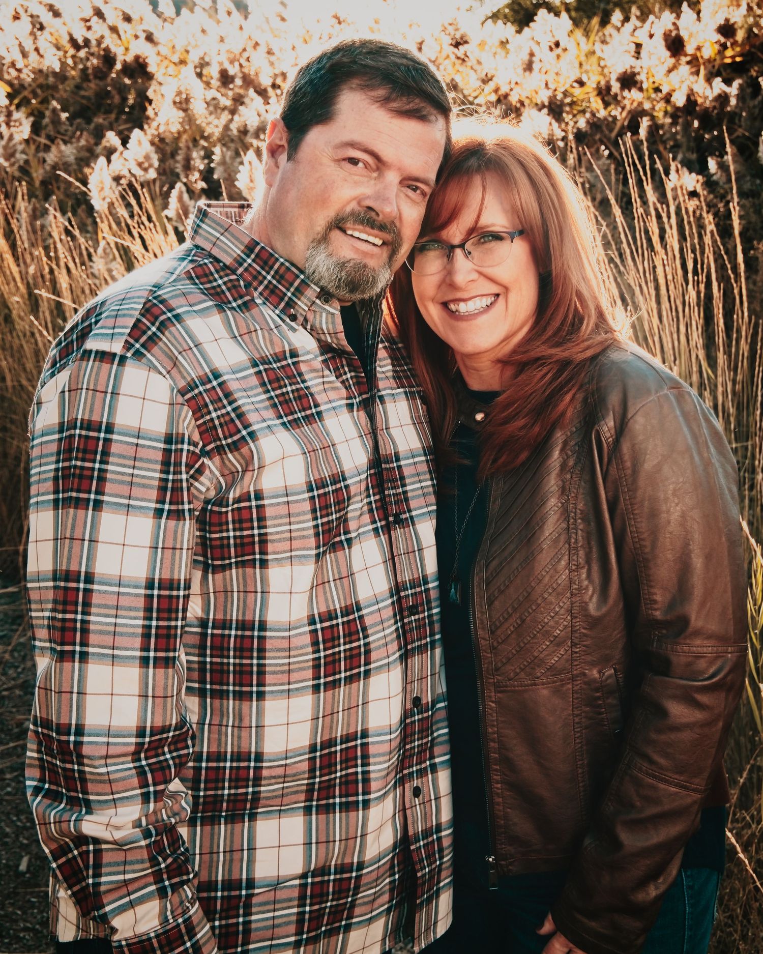 A middle-aged couple stand with heads touching smiling at the camera
