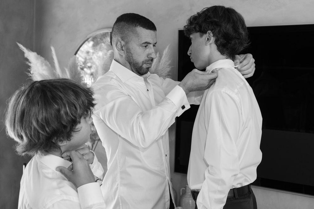 Black and white photo of family members adjusting formal wear before event.